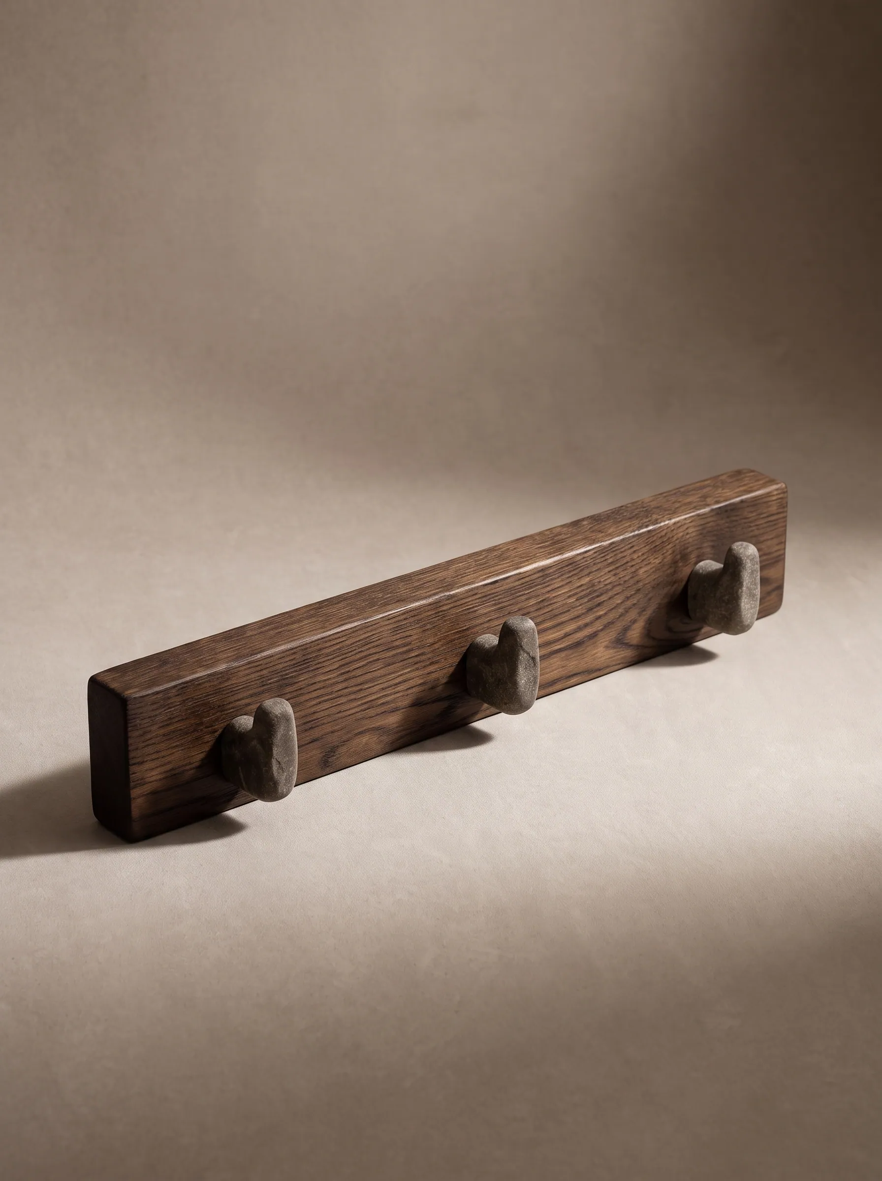A smoked-oak wall rail with three stone pegs on a beige ground
